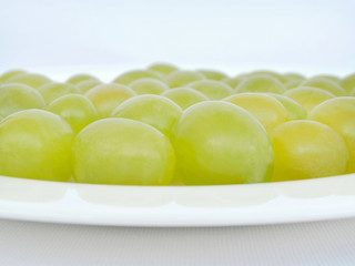Ripe juicy green grapes lying flattened on a white plate, light background, front view, close-up, copy space