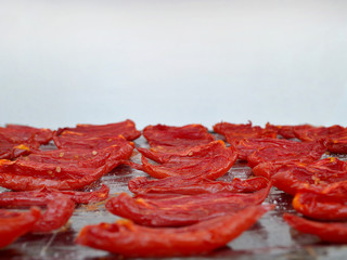 A lot of red homemade oven dried tomatoes on a black baking sheet pan on light background, close-up,  front view, copy space