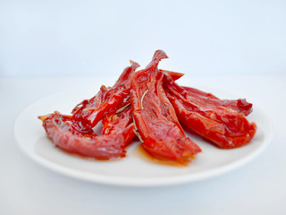 Red homemade oven dried tomatoes with rosemary on a white saucer against a light background, close-up, front view