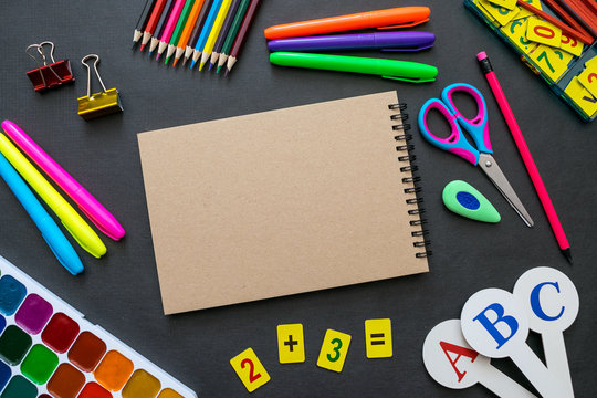 School supplies mockup on blackboard background with copyspace. Bright multicolored, pencils, pens, scissors, notepads, letters, figures, brushes, paints, clamps, eraser and other stationery