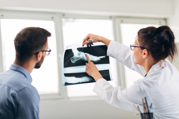 Fototapeta premium Portrait of Woman Doctor at her Medical Office Looking at X-Ray with Patient
