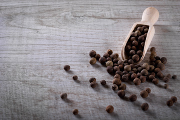 Pepper peas in a wooden spoon on a wooden background. Spices are scattered on the table