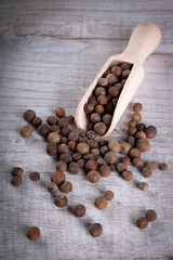Pepper peas in a wooden spoon on a wooden background. Spices are scattered on the table