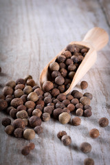 Pepper peas in a wooden spoon on a wooden background. Spices are scattered on the table