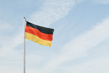 German flag developing in the wind against the blue sky.