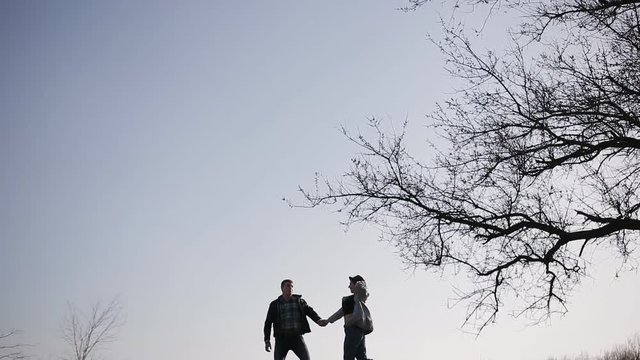The silhouettes of the fleeing lovers on the hill near the big tree at sunset