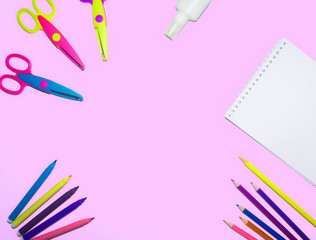 flat lay picture of colored pencils, notepad and scissors lined on a flat surface of an isolated pink background