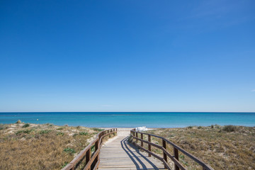 Wooden path leading to sandy beach on the Mediterranean Sea with clear blue water and sky
