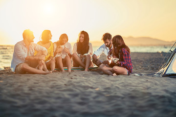 Young friends with guitar at beach. friends relaxing on sand at beach with guitar and singing on summer sunset.