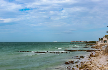 Fototapeta na wymiar View along eroded beach with sand fencing in Progreso Mexico toward the worlds longest pier that allows ships to dock in the shallow Gulf of Mexico but also causes erosion of the beaches
