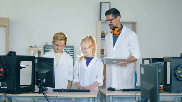A laboratory worker teaches kids how to work with a 3D printer.