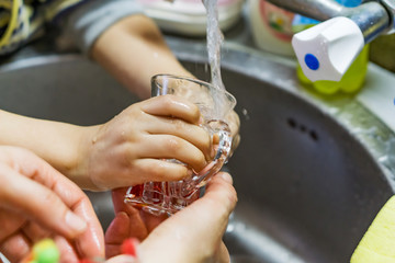 Close-up of the hands of a little boy filling a glass of water on the tap. Shallow depth of focus.