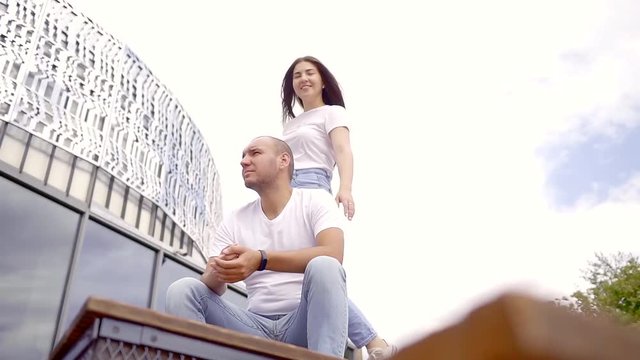 Man sitting on the stairs of a building and his woman coming from behing to him.