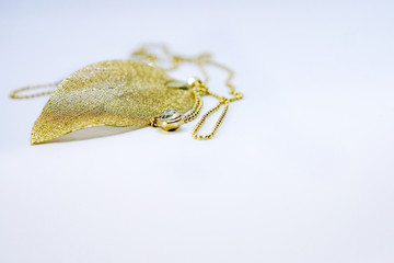 Close-up of gold necklace - autumn leaf with zirconia on white background. Shallow depth of focus. Concept fashion and beauty.