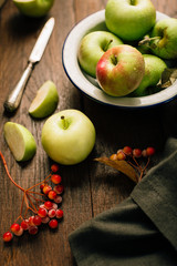 Green apples in a bowl on a wooden background, berries of a viburnum nearby, autumn still life