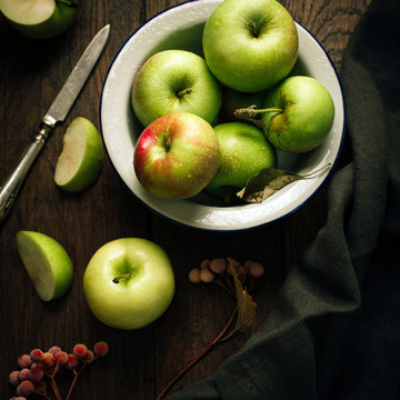 Green apples in a bowl on a wooden background, berries of a viburnum nearby, autumn still life