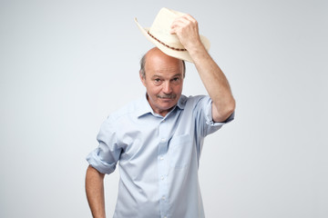 You are welcome concept. Cheerful mature man in blue shirt and cowboy hat gesturing welcome sign