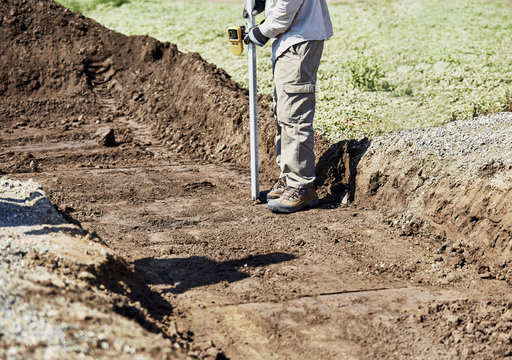Construction Worker Measuring The Depth Of A Newly Dug Trench