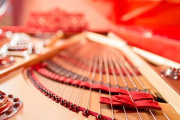 Strings inside a red grand piano. Piano playing, dampers, felt hammers, bronze strings and metal frame.