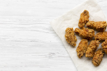 Fried chicken wings on baking paper sheet over white wooden background, top view. From above, overhead. Copy space.