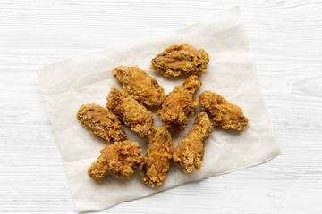 Fried chicken wings on baking paper sheet over white wooden background, top view. From above, overhead.