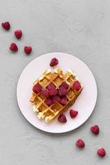 Traditional belgian waffle with raspberries on pink plate over gray background, view from above.