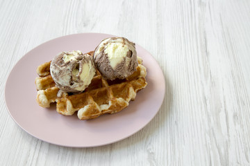 Traditional belgian waffle with icecream on pink plate, side view. White wooden table. Copy space.