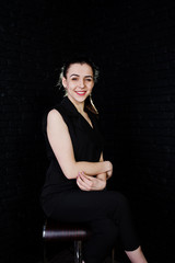 Portrait of a beautiful brunette girl in black jumpsuit sitting and posing in the studio.