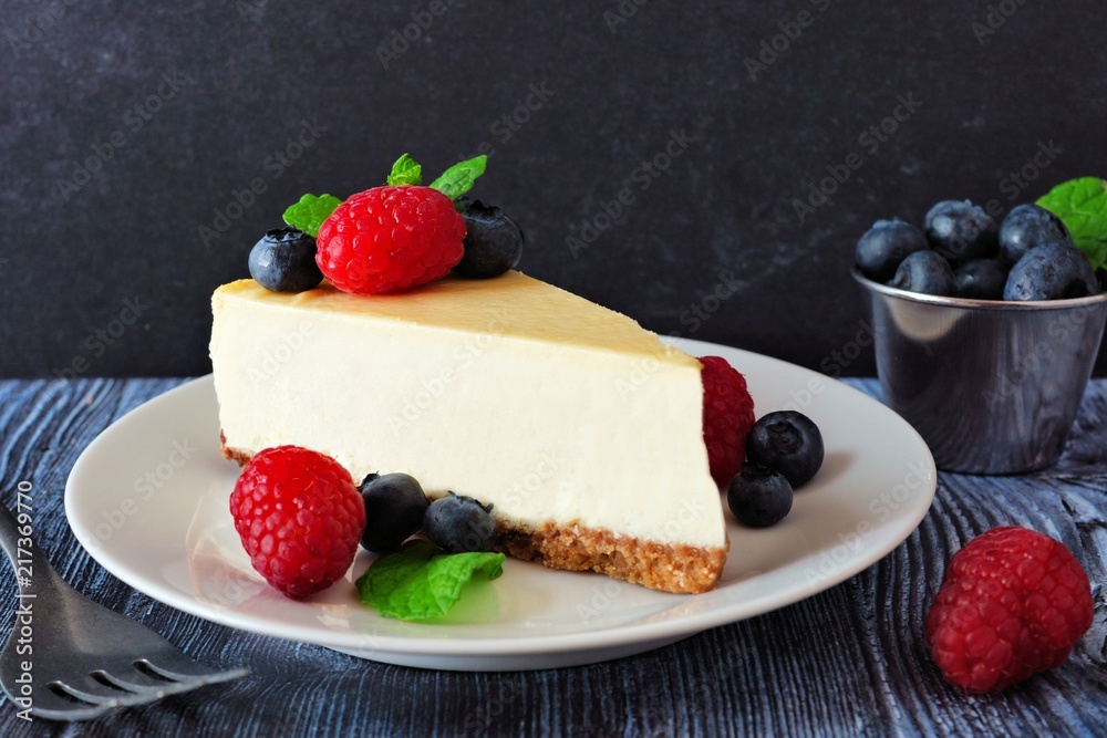 Poster slice of cheesecake with blueberries and raspberries on a plate, close up scene with a dark backgrou