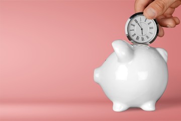 Hand depositing clock in piggy bank