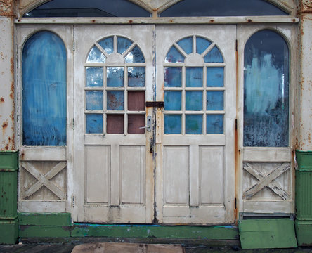 white wooden doors in an abandoned derelict house with broken and vandalized painted over windows