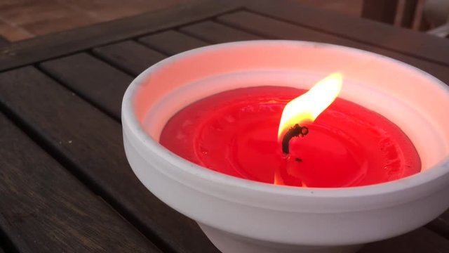 Red candle burning brightly on teak table top, mosquito repellant scented candle to summer insects