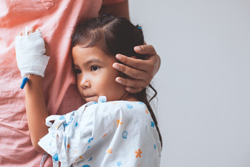 Sick asian little child girl who have IV solution bandaged hugging her mother with love in the hospital
