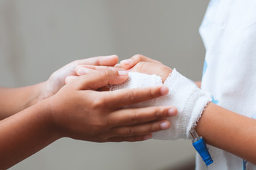 Child girl holding sick young sister hand who have IV solution bandaged with love and care in the hospital