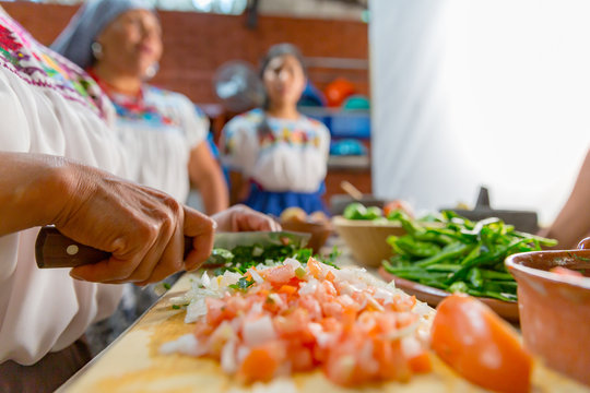 Mujeres en preparaci&oacute;n de alimentos, picando jitomate, cebolla y chiles sobre una tabla en una cocina tradicional mexicana