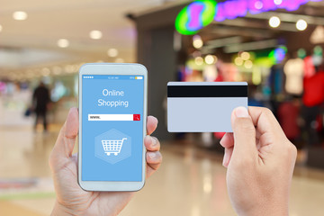 Hand holding smart phone with online shopping on screen and credit card over blurred in shopping mall background for mobile banking payment online concept