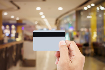 Man hand holding credit card on blur of shopping mall with shining bokeh lights for credit card payment concept