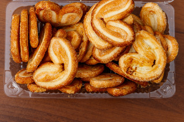 Palmier biscuits - french cookies made of puff pastry (also called palm leaves, elephant ears or french hearts) packed in plastic box on wooden table