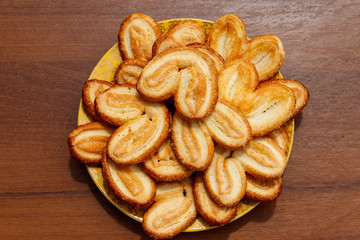 Palmier biscuits - french cookies made of puff pastry (also called palm leaves, elephant ears or french hearts) in a plate on wooden table
