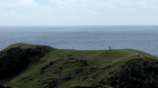 Tourists walking across the top of a hill with an endless ocean behind. Shot in Basco, Batanes.