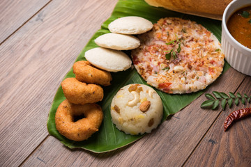 Group of South Indian food like Masala Dosa, Uttapam, Idli/idly, Wada/vada, sambar, appam, semolina halwa, upma served over banana leaf with colourful chutneys, selective focus