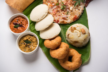 Group of South Indian food like Masala Dosa, Uttapam, Idli/idly, Wada/vada, sambar, appam, semolina halwa, upma served over banana leaf with colourful chutneys, selective focus