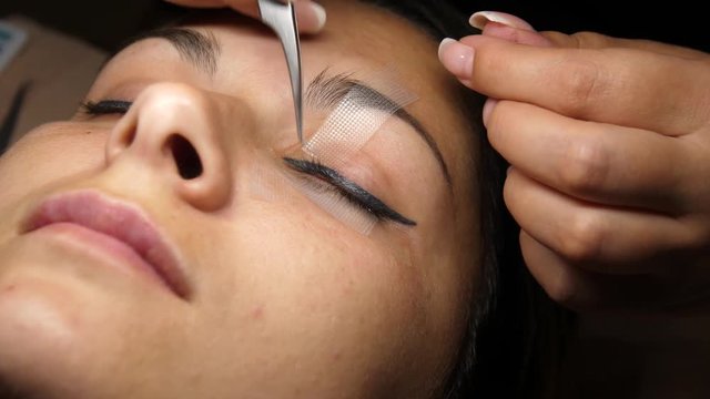 Beauty and fashion concept. Preparation for Eyelash Extension Procedure. Beautician prepares the eyelashes of a young woman to eyelash extension.