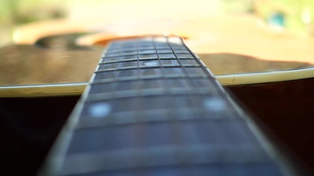Acoustic guitar with wooden finish in slow motion in nature and grassy riverside.