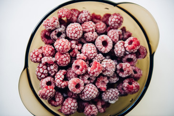 Frozen raspberries on a plate on white background lifestyle