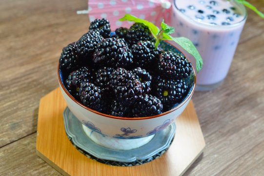 Close-up of  juicy blackberries in a bowl on rustic table and milk and berry milkshake

