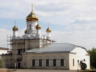 Mozhaisk, Russia - Old white Church with Golden domes, crosses and Annex in the city center, the city landscape on a summer day against the blue sky with clouds, restoration, scaffolding