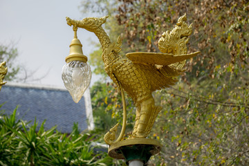 bronze casting Thai literature swans carrying bell-shaped electricity lantern painted with gold colour located in the Wat Pha Phu Gon temple's garden.