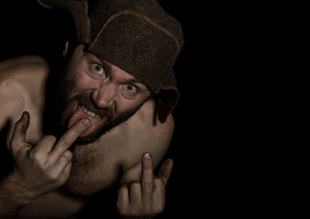 frightening bearded man showing middle finger. strange Russian man with a naked torso and a woolen...