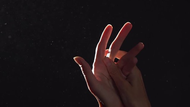 Silhouette Portrait Of Two Beautiful Female Arms Closeup Massaging And Rubbing Hands In Light With Flying Dust Into Air, Isolated Over Black Background